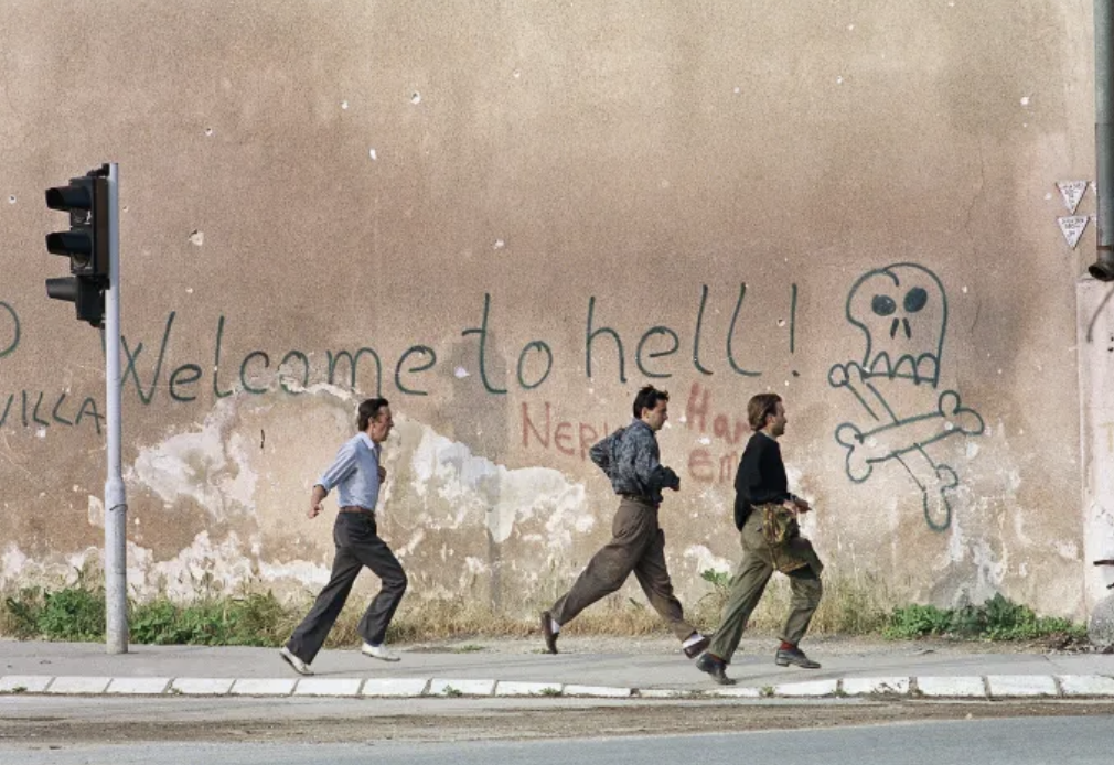 Three men run for cover past graffiti reading: 'Welcome To Hell' as sniper fire rings out along Sarajevo's notorious 'sniper alley' Wednesday, June 9, 1993 in Sarajevo [Peter Northall/AP]